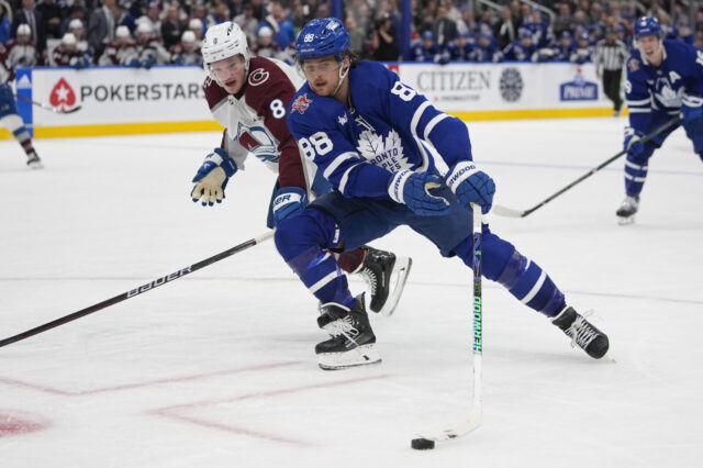 William Nylander for the Toronto Maple Leafs skates holding the puck away from the Colorado Avalanche's Cale Makar.